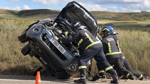 Unos bomberos levantan el coche volcado en la cuneta de la carretera.