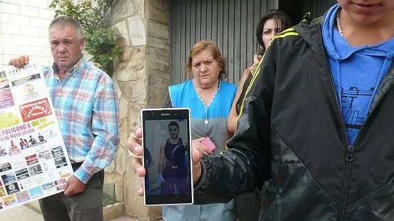 Un joven muestra una imagen del desaparecido, con el padre de éste al fondo.