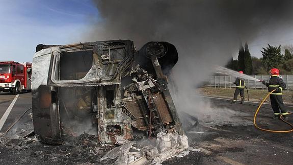 Dos bomberos extinguen el fuego del camión siniestrado. 