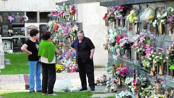 Tres personas conversan en el cementerio de Guardo ante los nichos adornados con flores.