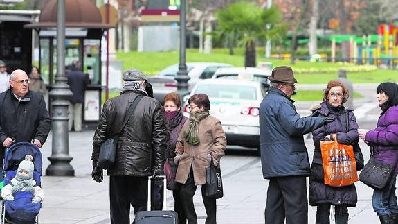 Un hombre camina con una maleta en el inicio de la Calle Mayor, donde otras personas pasean y conversan.