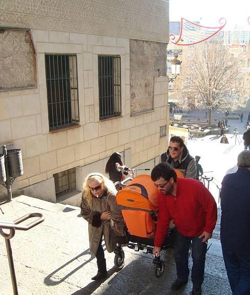 Una pareja carga con un carrito de bebé ayudada por una tercera persona.