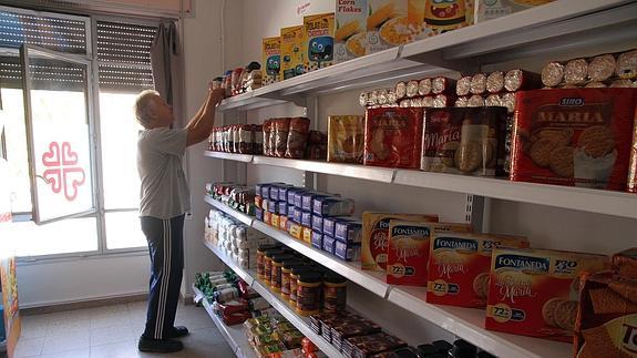 Un hombre coge un paquete de comida de una de las estanterías del economato de Cáritas.