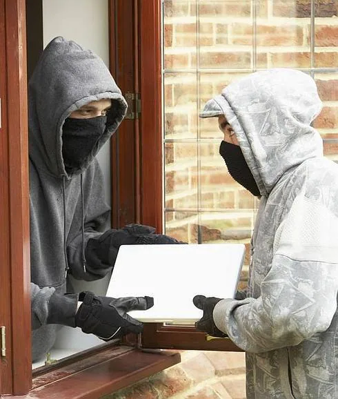 Ladrones robando un ordenador portátil por la ventana.