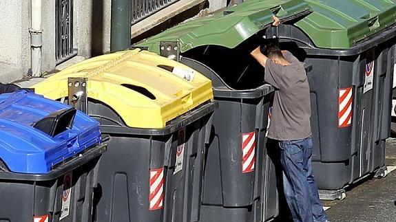 Un hombre busca algo aprovechable entre la basura de un contenedor.