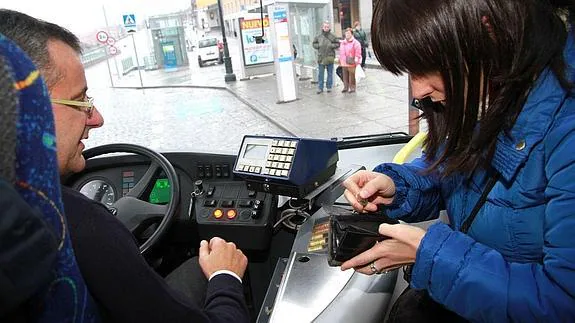 Una joven paga el billete en un autobús de transporte urbano.
