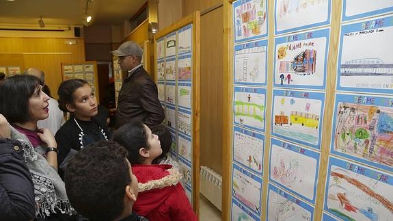 Una mujer y unos niños observan los dibujos de la exposición sobre el aislamiento de Pilarica.