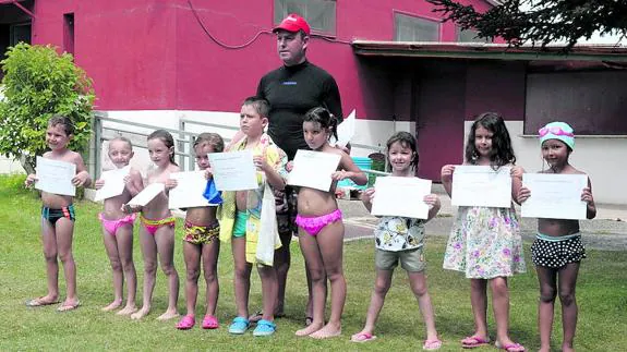 El socorrista de Olombrada, Alfonso de la Fuente, entrega los diplomas a los a los niños participantes en el primer cursillo de natación de este verano. 