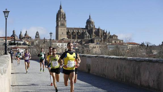 Un grupo de corredores pasa por el Puente Romano de Salamanca con las catedrales al fondo. 
