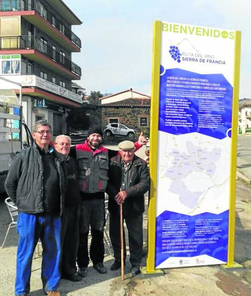 Varias personas junto al cartel de la Ruta del Vino ubicado en Sotoserrano. 