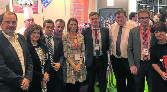 Representantes de las instituciones de Saborea Segovia posan con productores y visitantes del espacio dedicado a la provincia y, a la derecha, preparativos para la degustación de cochinillo. 