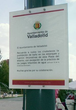 Dos jóvenes se refrescan junto al cartel que prohíbe hacerlo en los chorros decorativos de la plaza del Milenio. ::                             J. S.