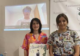 La concejala sujeta al cartel ganador junto a la profesora con la foto del alumno en la pantalla.
