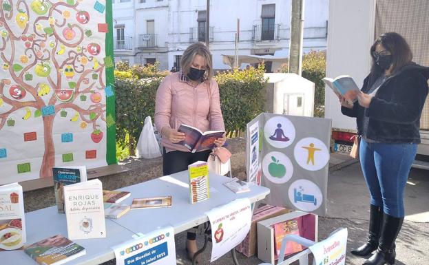 Imagen principal - Dos vecinas de la localidad ojean libros sobre salud durante la Feria de la Salud. 