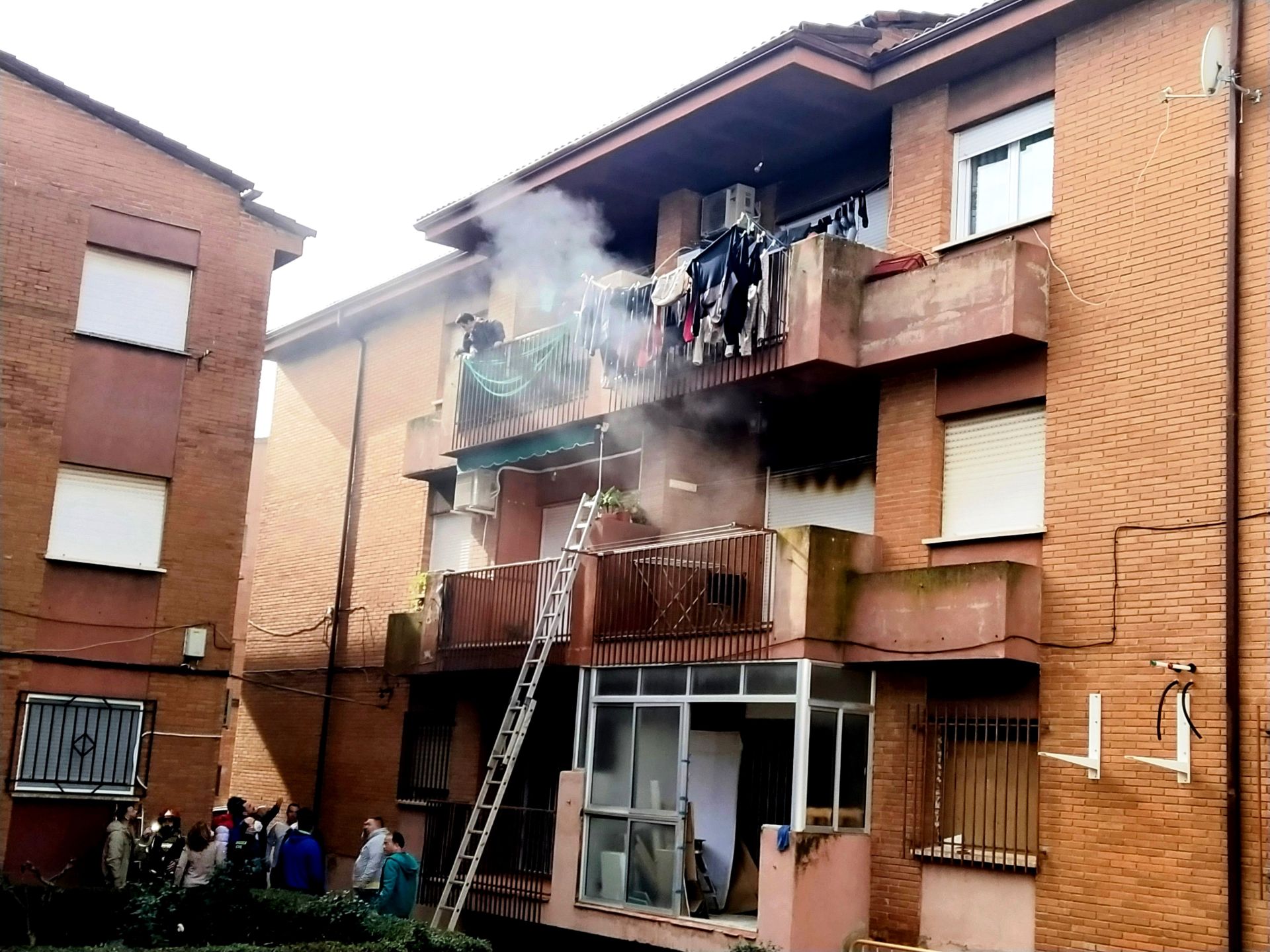 Evacuación de los vecinos en la parte de atrás y piso siniestrado en la parte derecha con las ventanas cerradas.