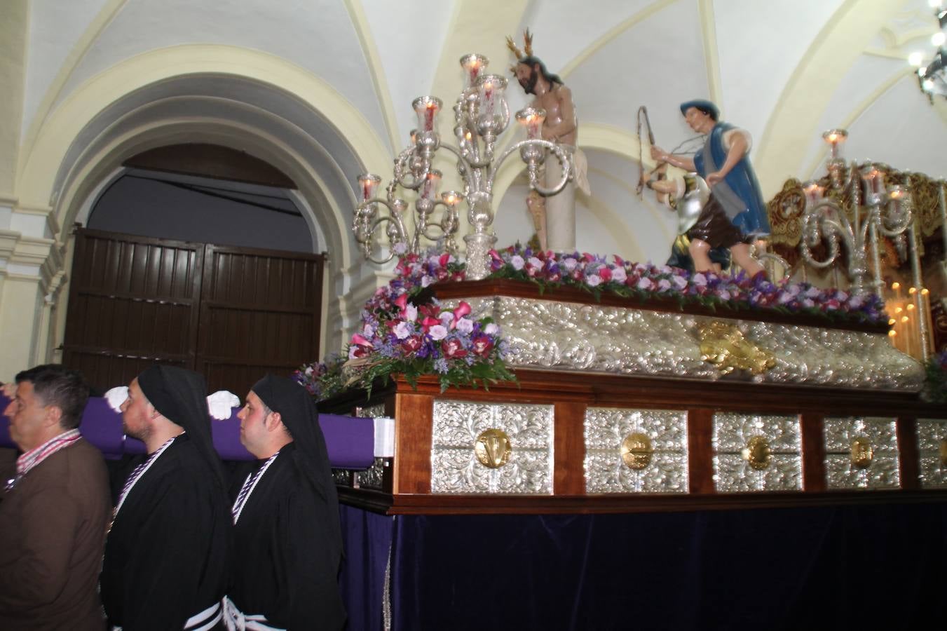 Las emociones llenaron también anoche la ermita de Los Santos Mártires, donde se quedaron guardados todos los afanes, las ilusiones y la devoción que no pudieron tener reflejo en la procesión de las colas largas, La Cofradía del Señor Coronado de Espinas decidió no salir ante la adversidad de la climatología y en el interior de este pequeño templo se vivieron momentos de gran emotividad.La Guardia Civil de Jerez de los Caballeros rindió honores a s Madrina, María Santísima de la Amargura. Los sones de las bandas y agrupaciones que iban a participar en el desfile procesional expandieron su eco desde el Llano de los Mártires para acompañar a los costaleros de cada uno de los tres Pasos, que fueron mecidos a su compás. El jovencísimo saetero Julián Jaramillo, de tan solo 12 años y natural de Segura de León, hizo vibrar a los presentes con su saeta al Coronado.Y entre las oraciones del párroco, Antonio María Rejano y los sacerdotes que le acompañaron, asomaron también las lágrimas.El momento más emotivo se vivió con el sentido homenaje a Manuel Labrador González, Manolo 'Cornelio' a quien Marisa Sánchez, en nombre de la junta de gobierno de la Cofradía del Señor Coronado, dedicó palabras llenas de afecto y reconocimiento, destacando su condición de «trabajador sin igual», su carácter innovador, su generosidad, sus consejos a jóvenes y mayores en el seno de esta Cofradía de la que dijo, «es piedra angular» y su extraordinaria labor. Manuel recibió un libro y una precioso cartel realizada por José Tomás Pérez Indiano, a semejanza del que hace tres años anunció la Semana Santa Jerezana. Emocionado, Manuel agradeció el cariño y dedicó este homenaje a su familia y a todas las madres.