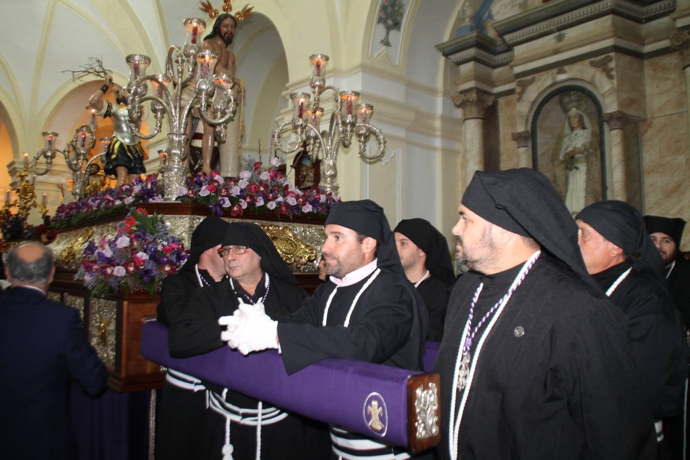 Las emociones llenaron también anoche la ermita de Los Santos Mártires, donde se quedaron guardados todos los afanes, las ilusiones y la devoción que no pudieron tener reflejo en la procesión de las colas largas, La Cofradía del Señor Coronado de Espinas decidió no salir ante la adversidad de la climatología y en el interior de este pequeño templo se vivieron momentos de gran emotividad.La Guardia Civil de Jerez de los Caballeros rindió honores a s Madrina, María Santísima de la Amargura. Los sones de las bandas y agrupaciones que iban a participar en el desfile procesional expandieron su eco desde el Llano de los Mártires para acompañar a los costaleros de cada uno de los tres Pasos, que fueron mecidos a su compás. El jovencísimo saetero Julián Jaramillo, de tan solo 12 años y natural de Segura de León, hizo vibrar a los presentes con su saeta al Coronado.Y entre las oraciones del párroco, Antonio María Rejano y los sacerdotes que le acompañaron, asomaron también las lágrimas.El momento más emotivo se vivió con el sentido homenaje a Manuel Labrador González, Manolo 'Cornelio' a quien Marisa Sánchez, en nombre de la junta de gobierno de la Cofradía del Señor Coronado, dedicó palabras llenas de afecto y reconocimiento, destacando su condición de «trabajador sin igual», su carácter innovador, su generosidad, sus consejos a jóvenes y mayores en el seno de esta Cofradía de la que dijo, «es piedra angular» y su extraordinaria labor. Manuel recibió un libro y una precioso cartel realizada por José Tomás Pérez Indiano, a semejanza del que hace tres años anunció la Semana Santa Jerezana. Emocionado, Manuel agradeció el cariño y dedicó este homenaje a su familia y a todas las madres.