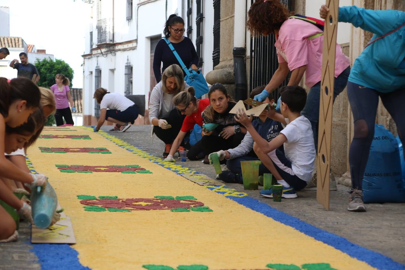Las alfombras de sal embellecen y llenan de color, hoy, las calles de Jerez de los Caballeros con motivo de la festividad del Corpus Christi. Desde primera hora de la mañana, miembros de las cofradías y hermandades, Cáritas, grupos de catequesis, familias de los niños que han hecho este año la Primera Comunión, miembros de la Asociación de costaleros y costaleras de la Semana Santa jerezana, Ayuntamiento y vecinos han cubierto las principales calles del municipio con 6.250 kilos de sal teñida, plenas de color. A continuación, han disfrutado de una jornada de convivencia en la Casa de la Iglesia 'Cecilia de Arteaga'.