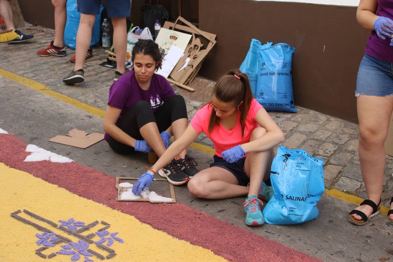 Las alfombras de sal embellecen y llenan de color, hoy, las calles de Jerez de los Caballeros con motivo de la festividad del Corpus Christi. Desde primera hora de la mañana, miembros de las cofradías y hermandades, Cáritas, grupos de catequesis, familias de los niños que han hecho este año la Primera Comunión, miembros de la Asociación de costaleros y costaleras de la Semana Santa jerezana, Ayuntamiento y vecinos han cubierto las principales calles del municipio con 6.250 kilos de sal teñida, plenas de color. A continuación, han disfrutado de una jornada de convivencia en la Casa de la Iglesia 'Cecilia de Arteaga'.