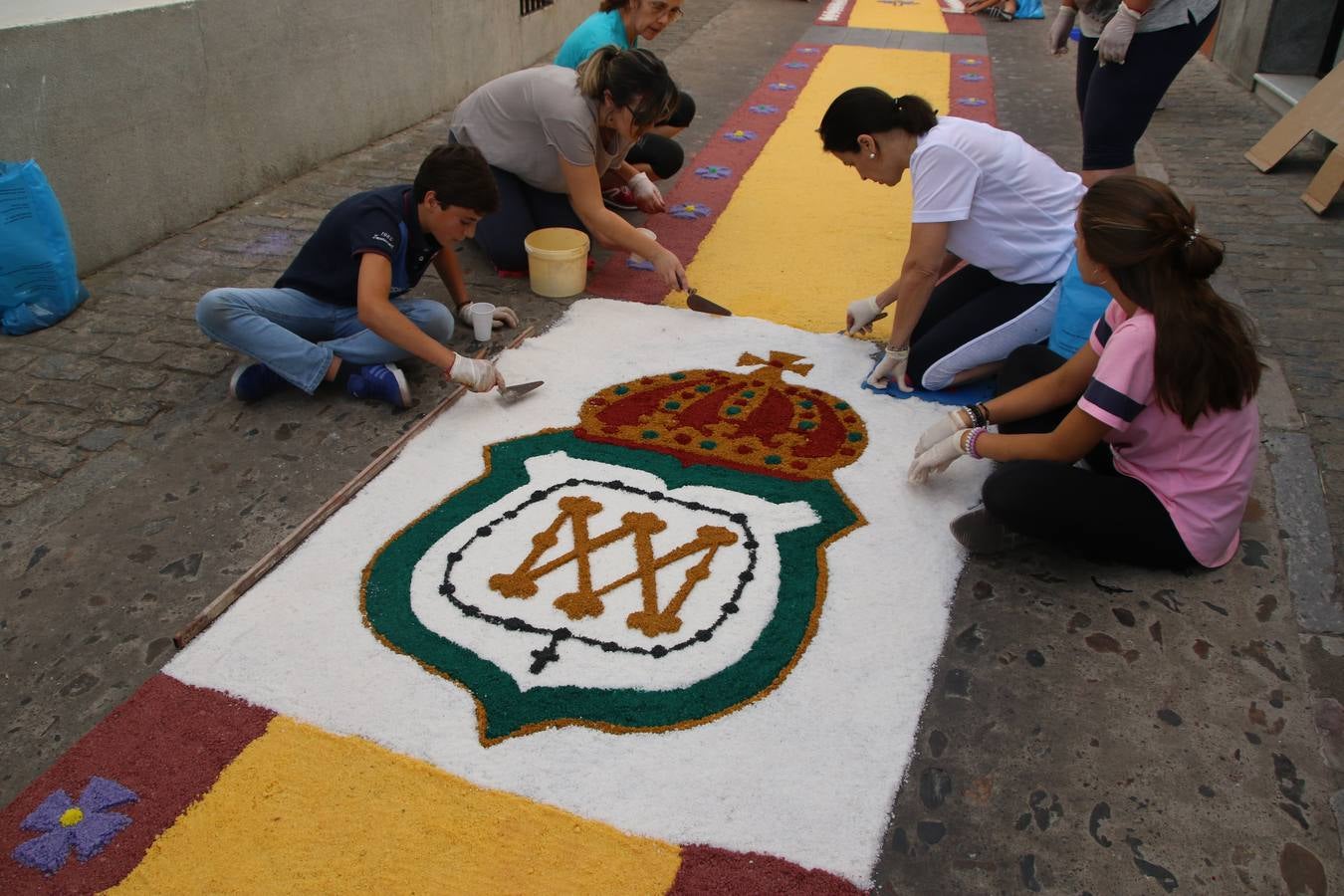 Las alfombras de sal embellecen y llenan de color, hoy, las calles de Jerez de los Caballeros con motivo de la festividad del Corpus Christi. Desde primera hora de la mañana, miembros de las cofradías y hermandades, Cáritas, grupos de catequesis, familias de los niños que han hecho este año la Primera Comunión, miembros de la Asociación de costaleros y costaleras de la Semana Santa jerezana, Ayuntamiento y vecinos han cubierto las principales calles del municipio con 6.250 kilos de sal teñida, plenas de color. A continuación, han disfrutado de una jornada de convivencia en la Casa de la Iglesia 'Cecilia de Arteaga'.
