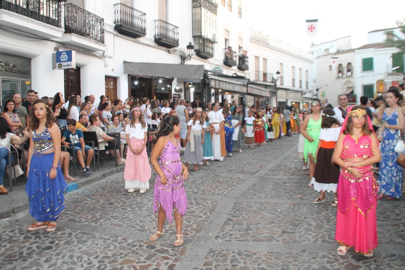 La participación popular fue nuevo protagonista del desfile teatralizado que anoche inauguró el grueso de la programación del XVI Festival Templario, invitando a propios y visitantes a revivir un pasado de leyenda, concretamente el siglo en el que La Orden del Temple marcó la vida de esta ciudad, en la que tuvo una de sus principales Encomiendas, siendo además el último reducto de Los Templarios en los reinos de España.La Asociación juvenil y cultural 'La Trouppe' estuvo al frente de la coordinación de dicho desfile que llenó de ambiente y animación las calles y plazas del centro histórico de Jerez de los Caballeros, llenas de público y engalanadas para la ocasión con pendones con la cruz templaria y otros elementos referentes a la cultura árabe que dejó su impronta en aquella época. Destacó la participación de más de 60 niñas que pusieron alegría con sus bailes a este pasacalle, junto a personajes fantásticos en zancos, la melodía de la Asociación Musical de Jerez de los Caballeros y la participación de asociaciones, como la del Belén 'Santa Ángela', Euexia Rural, además de los caballeros del campamento medieval a cargo de Cabalbur y de manera especial, la implicación de numerosos vecinos de todas las edades que desfilaron ataviados con indumentaria de la época dando vida a esta celebración.