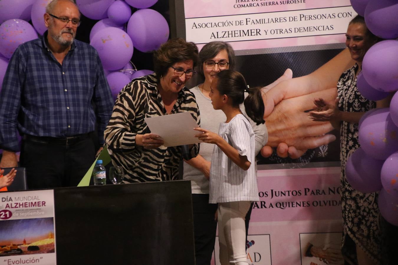 Ante las condiciones climatológicas adversas, el auditorio del Conventual San Agustín se convirtió en el mejor escenario para acoger las actividades que, con motivo del Día Mundial del Alzhéimer, la Asociación de Familiares de Personas con Alzheimer y otras Demencias de Jerez de los Caballeros y Comarca Sierra Suroeste (AFAD) había preparado en el municipio. Una gran pancarta con el lema 'Evolución', realizada por los alumnos del Colegio de Educación Especial 'Nuestra Señora de Aguasantas', presidió el escenario, y una marea de globos morados con distintos dibujos, realizados por los alumnos de los colegios 'Sotomayor y Terrazas' y 'El Rodeo', tiñó de color, empatía, sensibilidad y creatividad el citado auditorio.La jornada comenzó con la canción 'Estoy contigo' de la Oreja de Van Gogh. A continuación, tuvo lugar una mesa redonda en la que cinco personas contaron su testimonio en relación a esta enfermedad. Posteriormente, se dio paso a la lectura de un manifiesto; la entrega de diploma a las personas y colectivos colaboradores, y la lectura de dos cuentos infantiles.