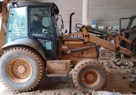 José Román ayudando a limpiar una nave con su máquina excavadora