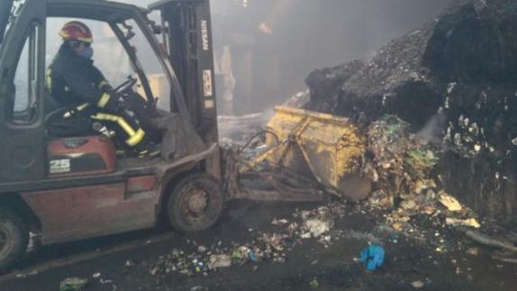 Un bombero recoge pacas de cartón comprimido del interior de la nave siestrada. 