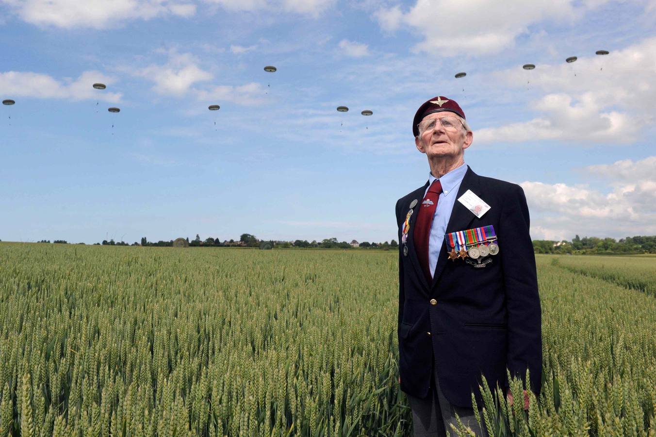 El veterano británico de la Segunda Guerra Mundial, Frederick Glover, posa para la fotografía mientras detrás los soldados se lanzan en paracaídas durante la exhibición realizada en Ranville, el norte de Francia. REUTERS / Thomas Bregardis.