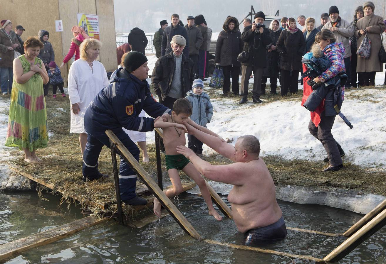 Un hombre entrega un niño a un socorrista después de bañarlo en las aguas heladas del río Bolshaya Almatinka durante la celebración de la Epifanía en Almaty. Los creyentes ortodoxos que respetan el calendario juliano marcan la Epifanía el 19 de enero. Fotografía: REUTERS-Shamil Zhumatov