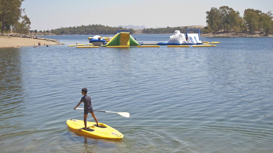 Un niño hace paddle surf junto a los columpios acuáticos.