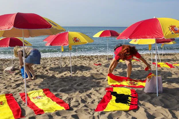 Banderas. Dos mujeres contrarias a la independencia de Cataluña colocan sombrillas y toallas en la playa del Prat.