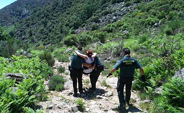 Tres agentes de la Guardia Civil del Servicio de Montaña llevan a una mujer que no puede caminar por un sendero de difícil acceso:: HOY