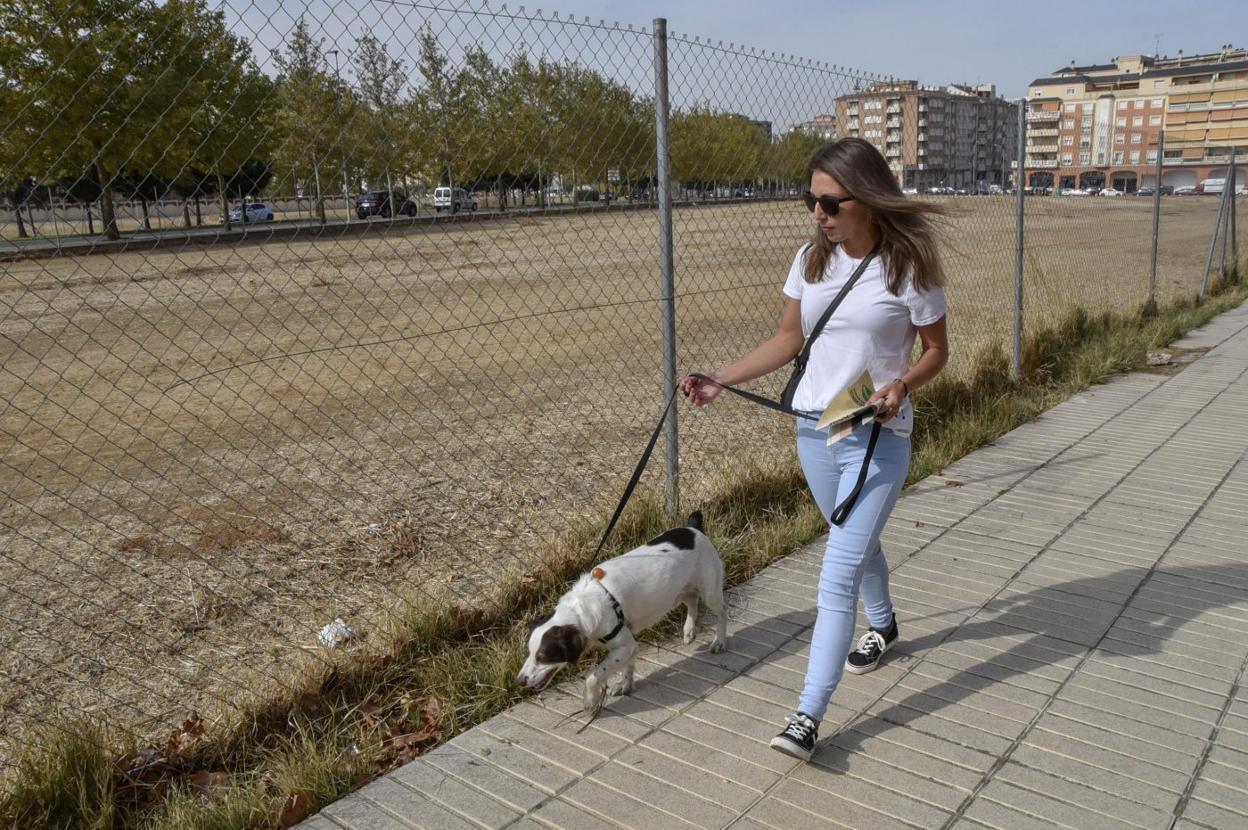 Una mujer, ayer, con su perro junto al solar municipal vallado cuyo acceso se ha precintado. :: Casimiro M.