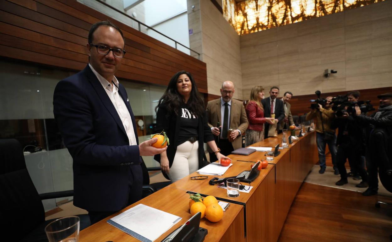 Cayetano Polo, en primer plano, sostiene una naranja en la Asamblea de Extremadura.