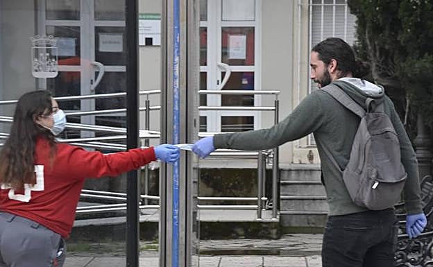 Una voluntaria de la Cruz Roja entrega una mascarilla esta mañana. 