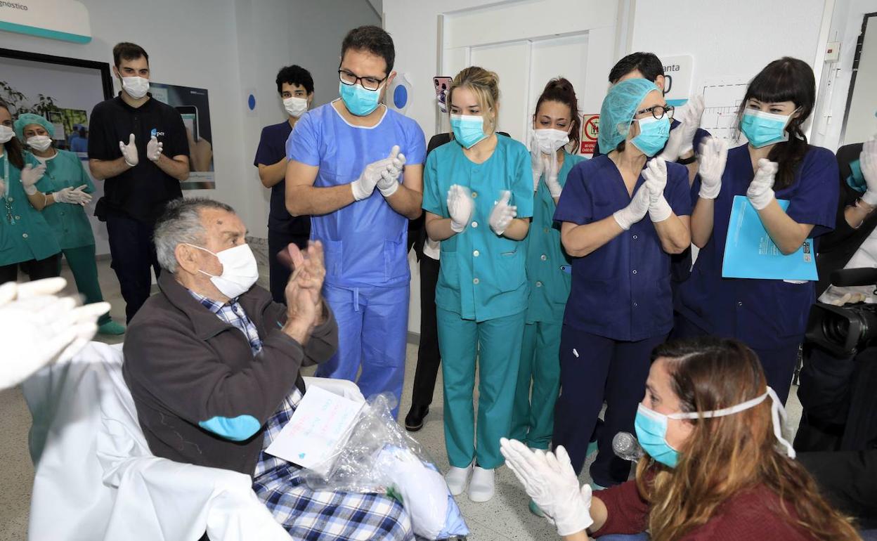 Feliciano Durán, de 85 años, besa las manos de su nieta mientras es aplaudido por el personal de la Clínica Quirón de Cáceres tras recibir el alta el 7 de abril. 