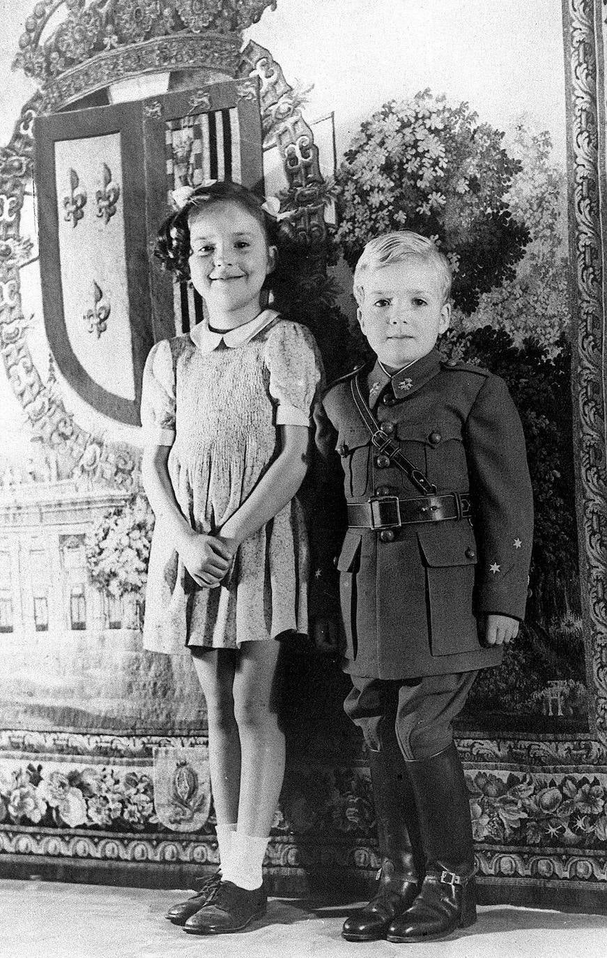 1942. El príncipe Juan Carlos de Borbón posa con el uniforme de capitán de caballería que le ha sido enviado de España, acompañada de su hermana, la infanta Pilar.