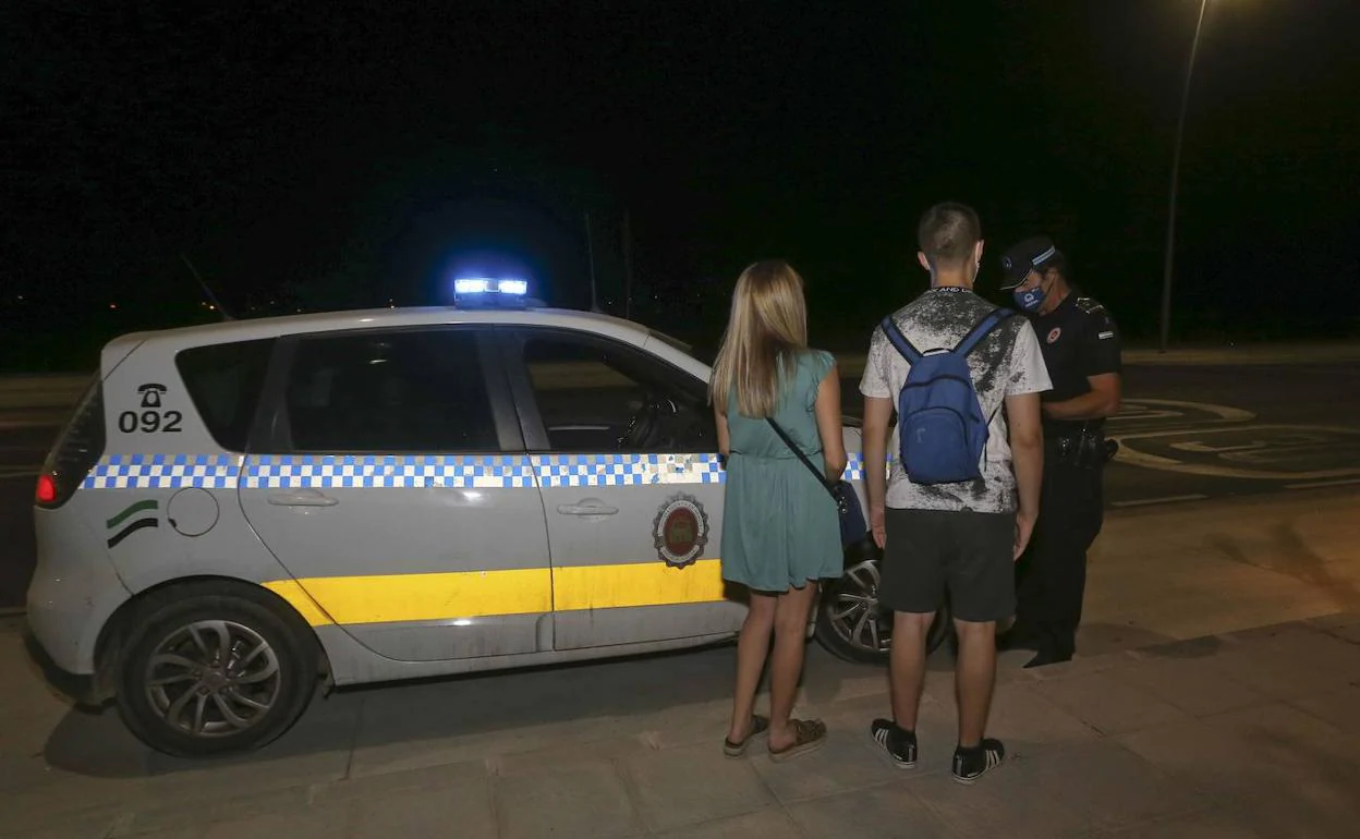 Un policía local multa a dos jóvenes por no llevar mascarillas.