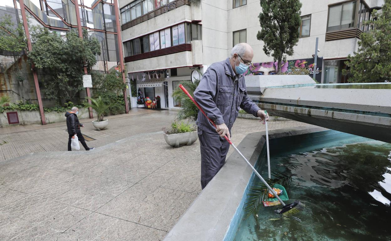 El portero de la finca recoge suciedad de la fuente central de la plaza de los Maestros. 