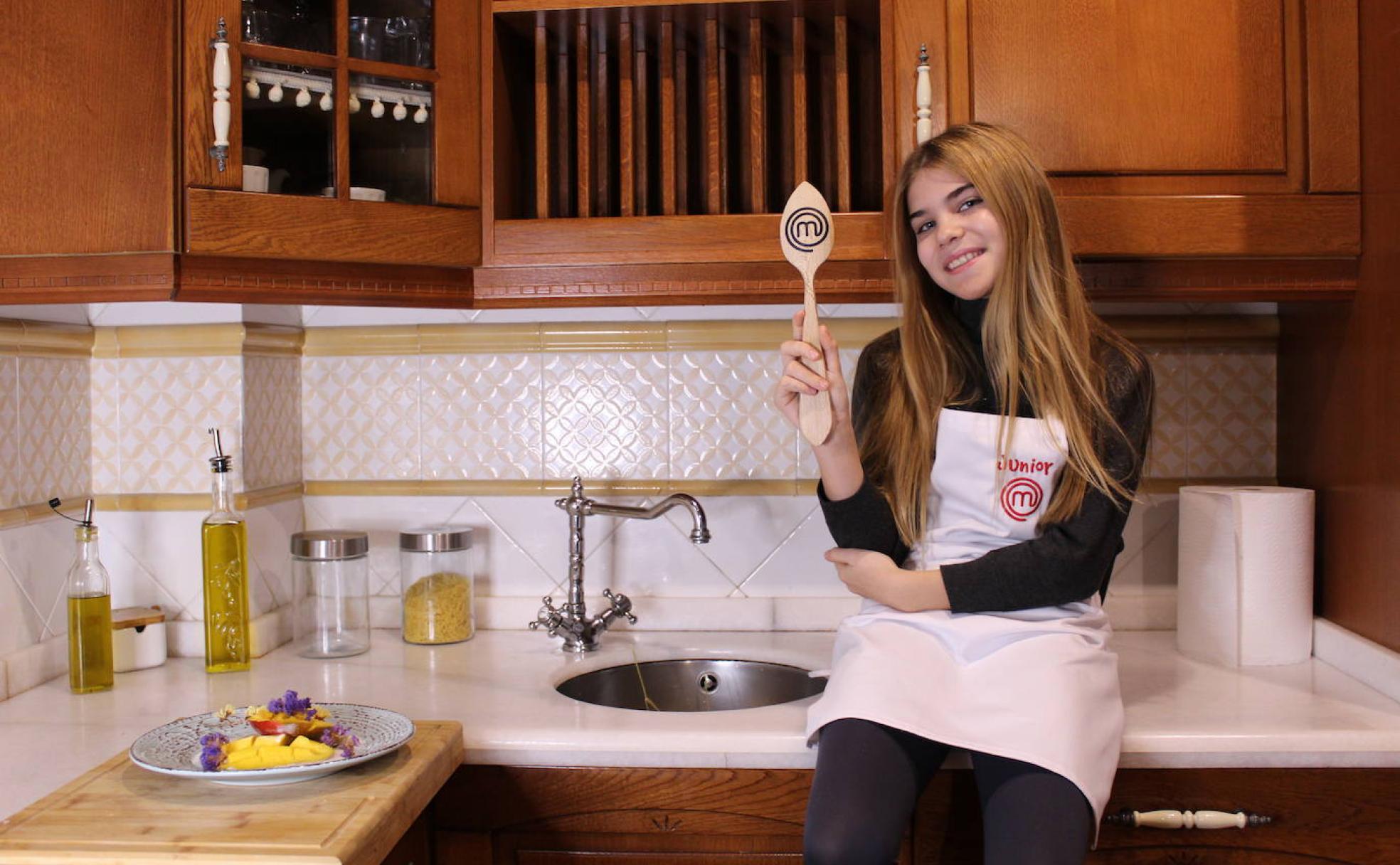 Celia posa con su cuchara y su delantal de MasterChef Junior en la cocina de su casa