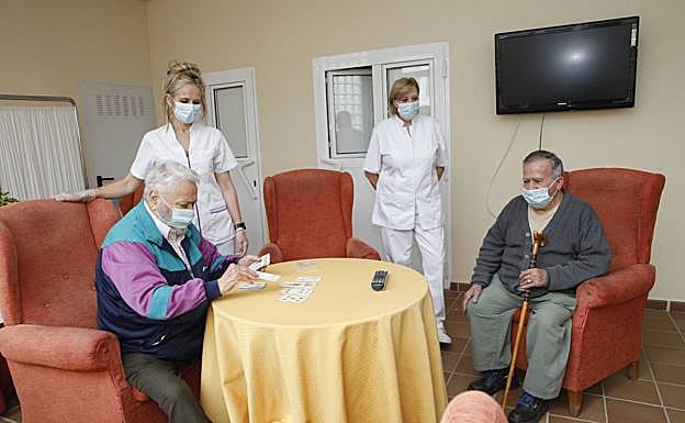 Dos auxiliares de la residencia en una de las salas mientras dos usuarios juegan a las cartas. 