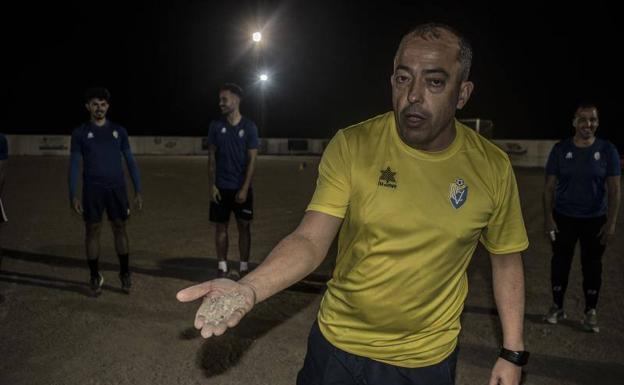 El técnico muestra la tierra y piedras del terreno de juego. Al fondo, la escasa iluminación. 