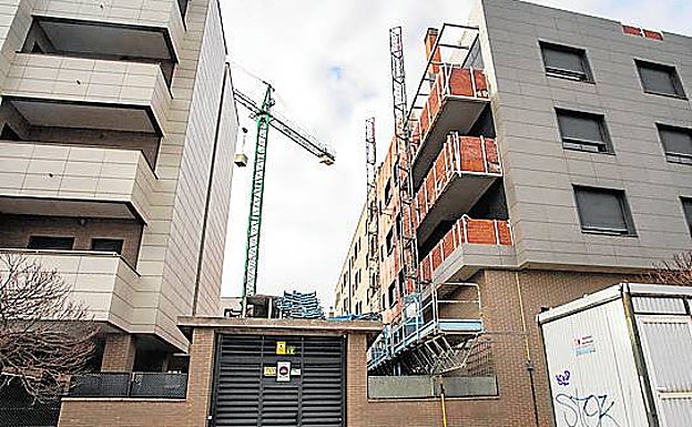 Edificio sin terminar junto al bloque habitado que completa una promoción, con una grúa en la zona de jardín, en Casa Plata.