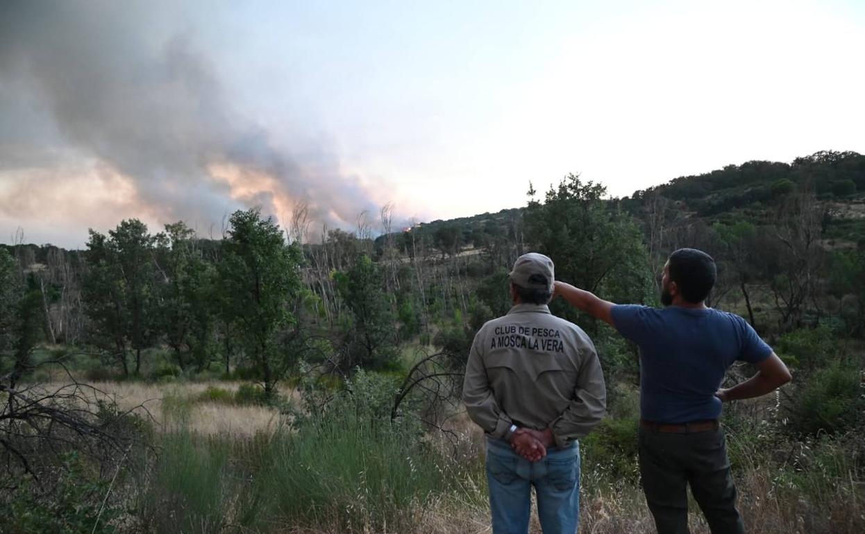 Dos hombres observan la evolución del incendio declarado este viernes cerca de Villanueva de la Vera. 