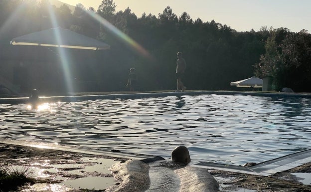 Un bañista al atardecer, relajando su cuello con el chorro de agua de manantial que llega hasta el vaso. 