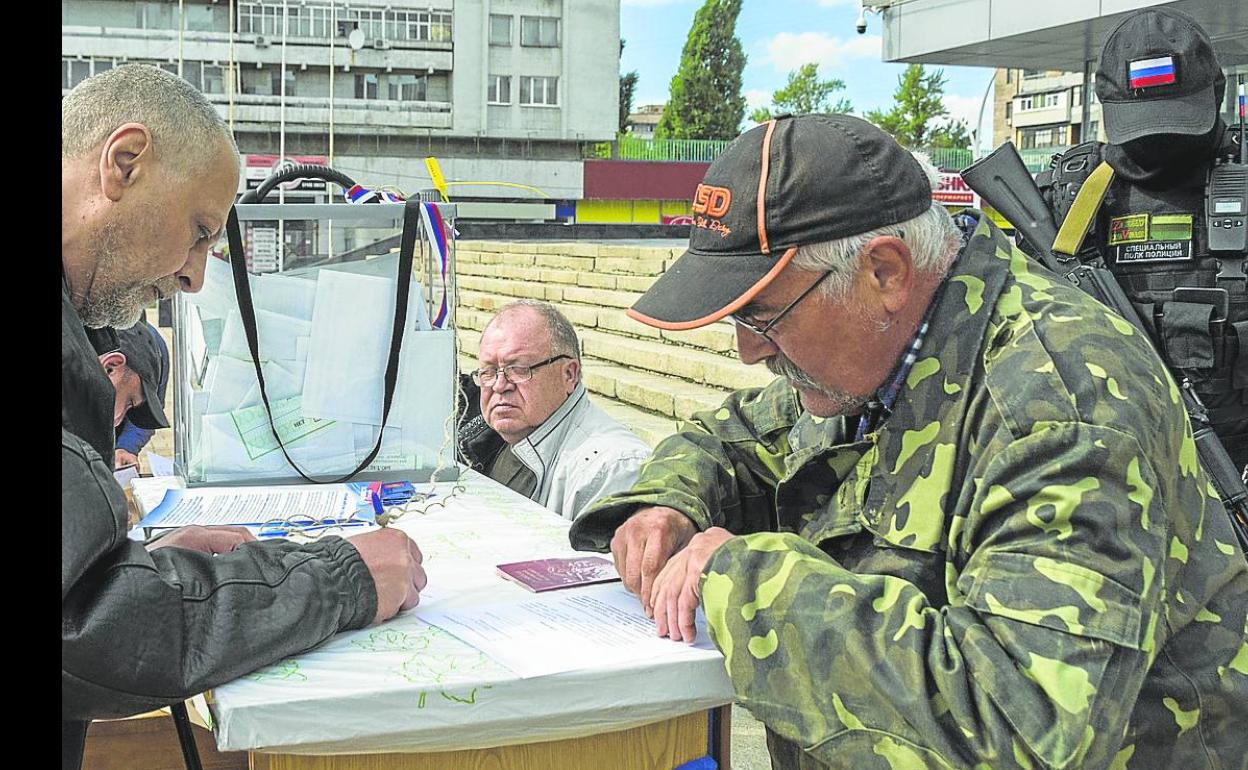 Un soldado ruso armado controla las votaciones en un colegio instalado en la calle en Lugansk. 