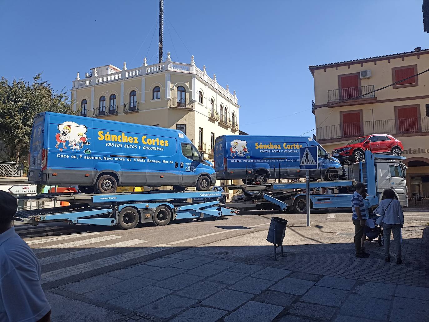 Un camión de transporte de vehículos pasa por Trujillo llevando dos furgonetas de la empresa Sánchez Cortés que ha cerrado.