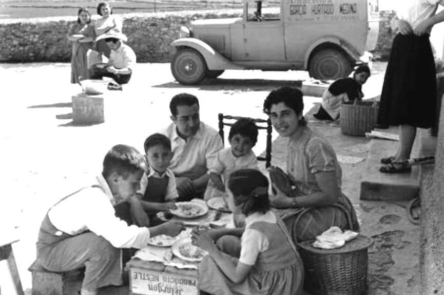 Familia comiendo sobre una caja de pelargón. Al fondo una furgoneta de Almacenes García Hurtado Medina.
