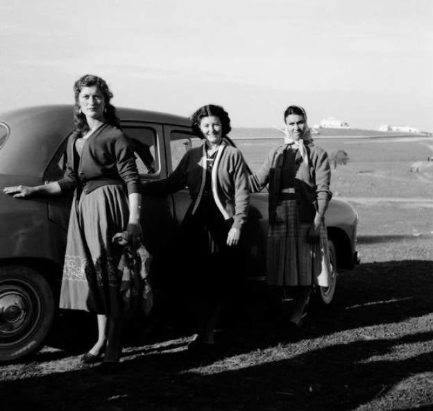 Tres mujeres posando en el campo junto a un coche.